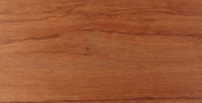 Bubinga lumber surface: orange to red-brown wood with dark streaks, close-up.