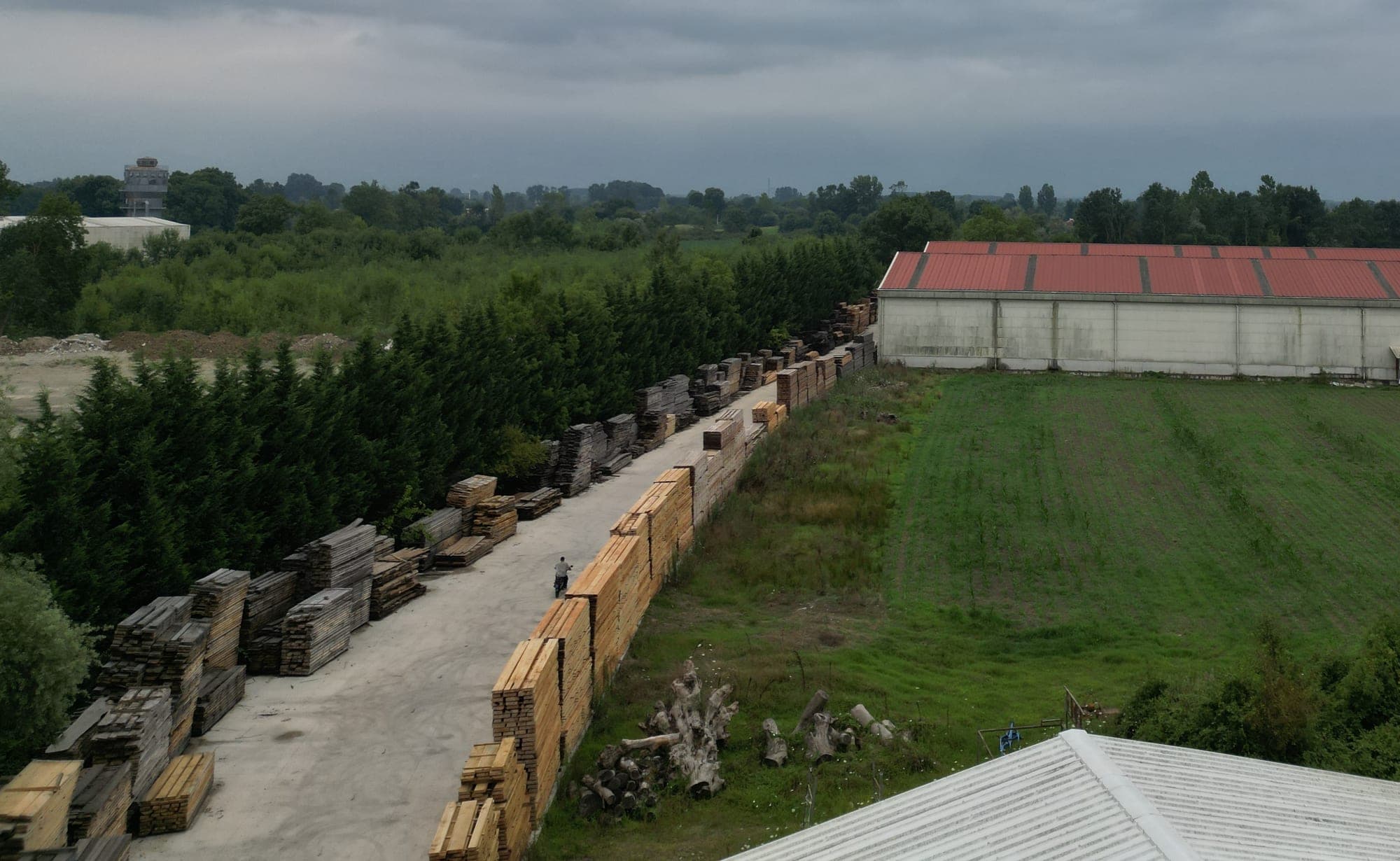 Lumber stacked along the yard road and the covered storage hall.