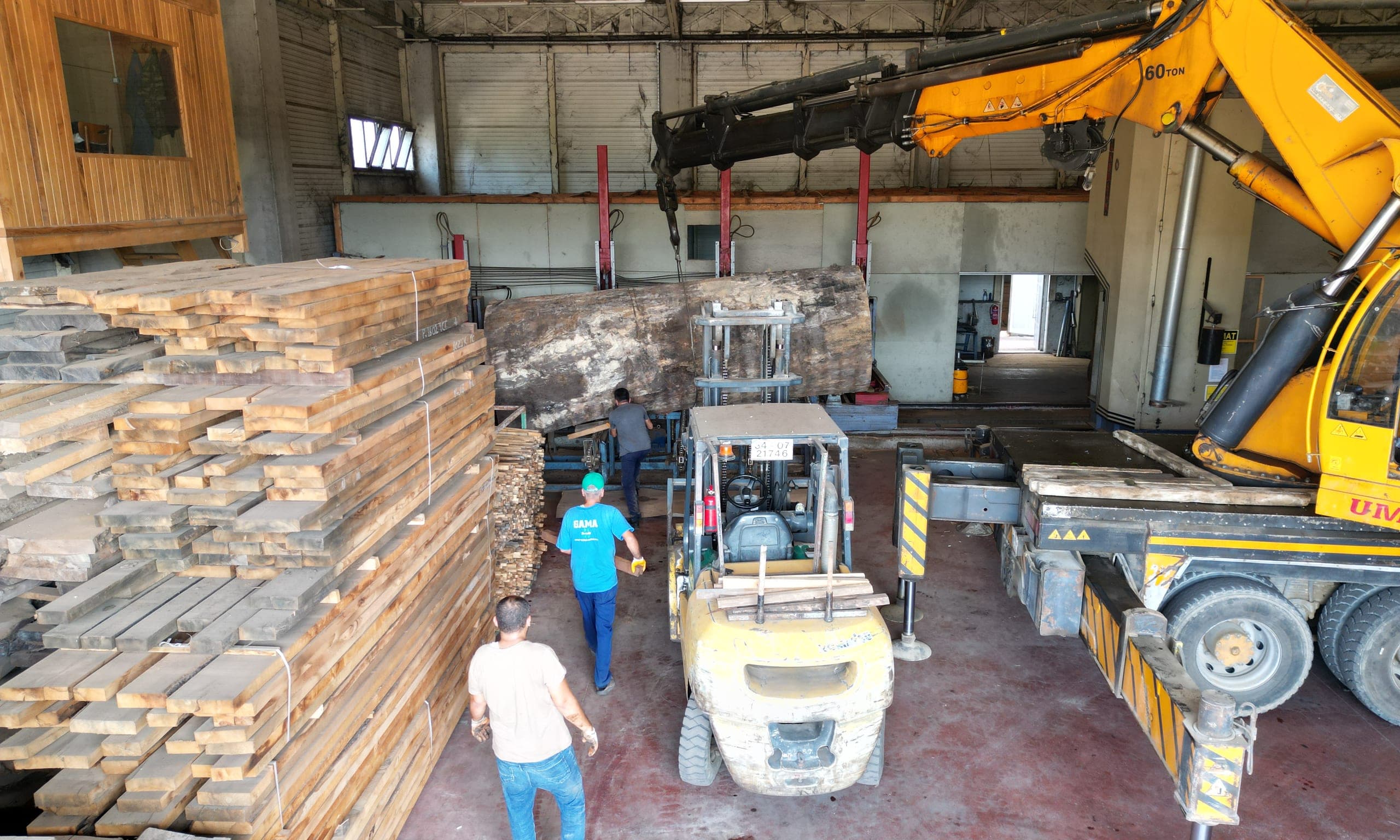 A large log being placed on the band saw by crane at our facility, with stacked lumber and a forklift in front.